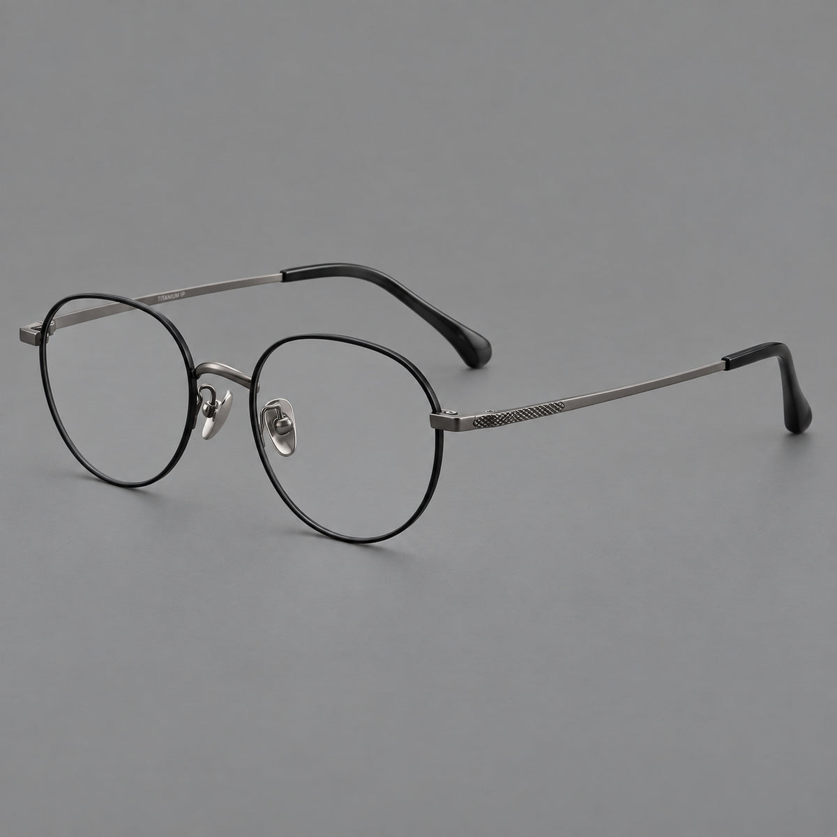 Compact round titanium glasses with an arched bridge and textured temple accents in Black and Gunmetal, three quarter view