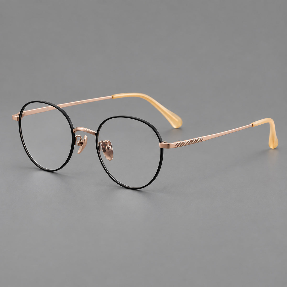 Compact round titanium glasses with an arched bridge and textured temple accents in Black and Rose Gold, three quarter view