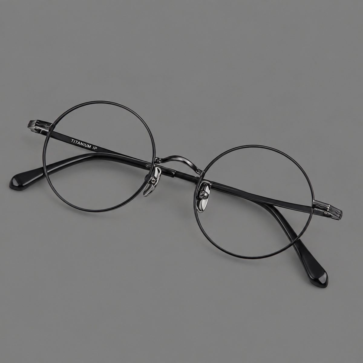 Compact circular titanium glasses with a curved bridge and wavy engraved temples in Black, three quarter view