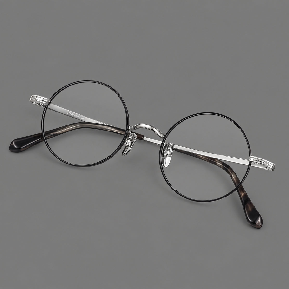 Compact circular titanium glasses with a curved bridge and wavy engraved temples in Black and Silver, three quarter view